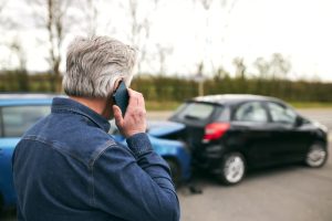 Senior man on phone at accident scene with rear-ended cars in the background.