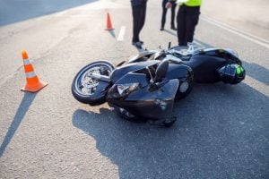 Overturned motorcycle on road after accident, surrounded by cones and two people.