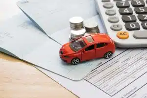 Red toy car on insurance documents with coins and calculator, symbolizing financial planning after accident.