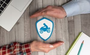 Hands framing a motorcycle insurance icon on a table with laptop and notebook.