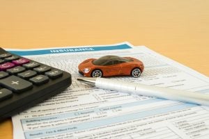 Toy car on insurance form with calculator and pen, symbolizing claim calculation.