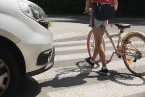 Cyclist with bike carefully crossing the street next to a car.