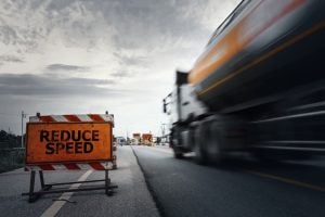 "Reduce Speed" sign on a road with a fast-moving truck passing by in blurred motion.