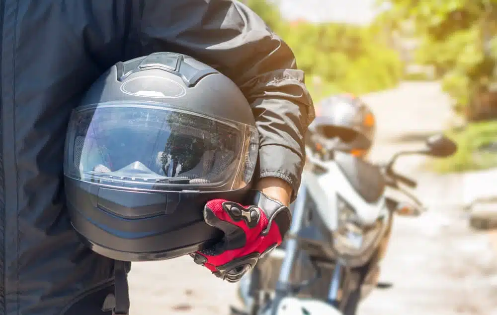 Motorcyclist holding helmet next to parked motorcycles on a sunny day.
