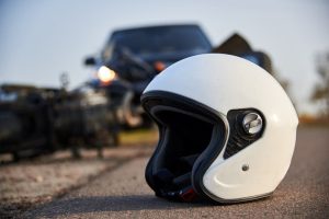 White motorcycle helmet in focus with overturned vehicle blurred in the background after crash.
