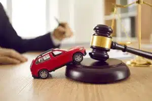 A small red toy car sits on a table next to a gavel and sound block, symbolizing car accidents, drunk driving, lawsuits, and legal services related to justice and court proceedings.
