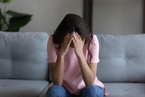A distressed woman sits on a couch with her head in her hands.