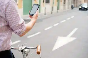 Cyclist holding a smartphone while stopped in a street with arrow markings.