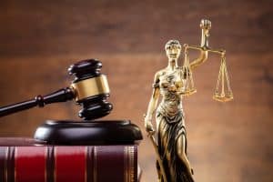 Close-up of a golden Lady Justice statue next to a wooden gavel resting on a law book.