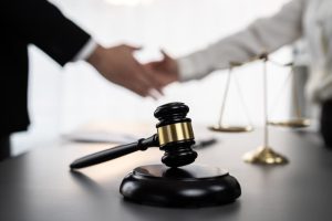 A gavel representing justice is in focus against a blurred background, where lawyers are shaking hands after a successful legal settlement to resolve a court dispute.