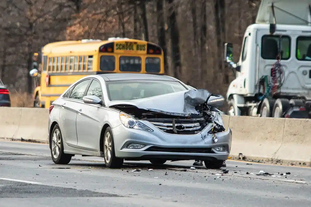 A silver car with significant front-end damage after a collision on a busy road.