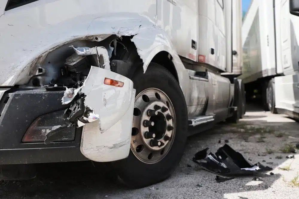 A damaged white truck with visible front-end collision damage and broken parts.