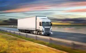 A white semi-truck driving on a highway at sunset with blurred motion.