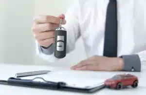 Man holding car key over a contract, with a pen and toy car.