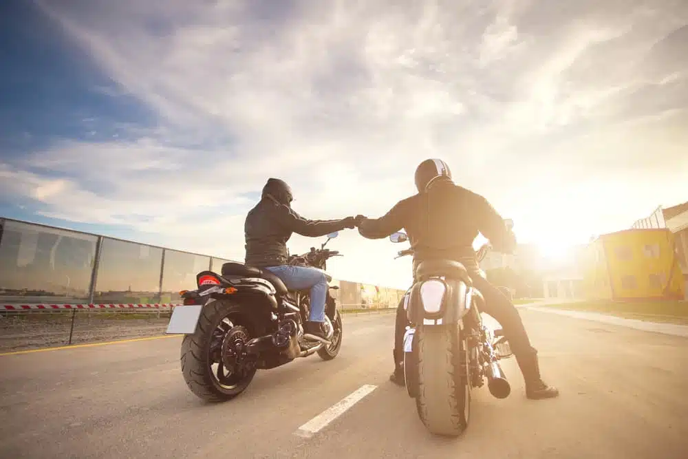 Two bikers ot motocycles handshaking with knuckle on road at sunshine