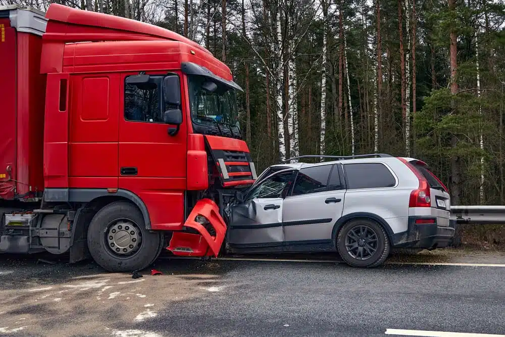 a collision between a large red semi-truck and a silver SUV on a road. The front of the truck has impacted the SUV's front, causing visible damage to both vehicles, particularly the SUV's hood and side.