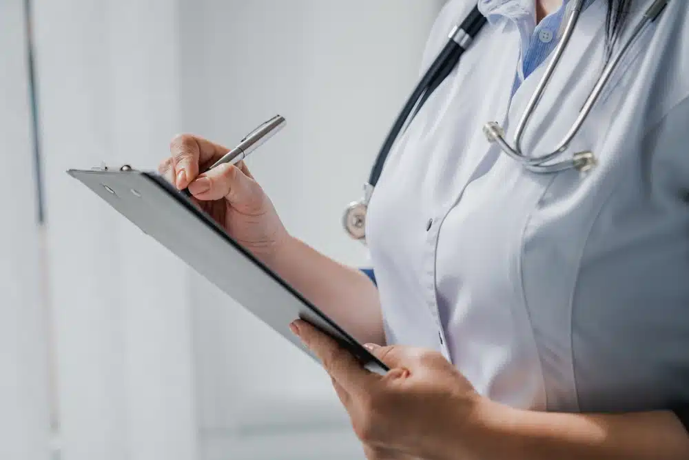 Female doctor with stethoscope writing prescription on clipboard.