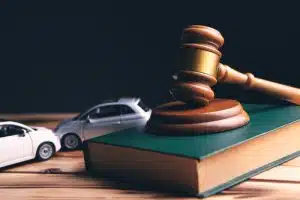 Gavel resting on a law book with toy cars beside it.