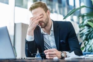 Man in a suit rubbing his forehead in frustration at a desk.