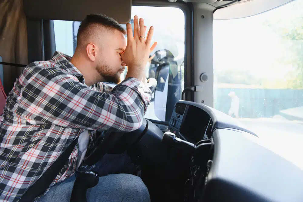 Truck driver sitting in the cab looking stressed, symbolizing the pressure and safety risks created by delivery quotas in commercial truck operations.