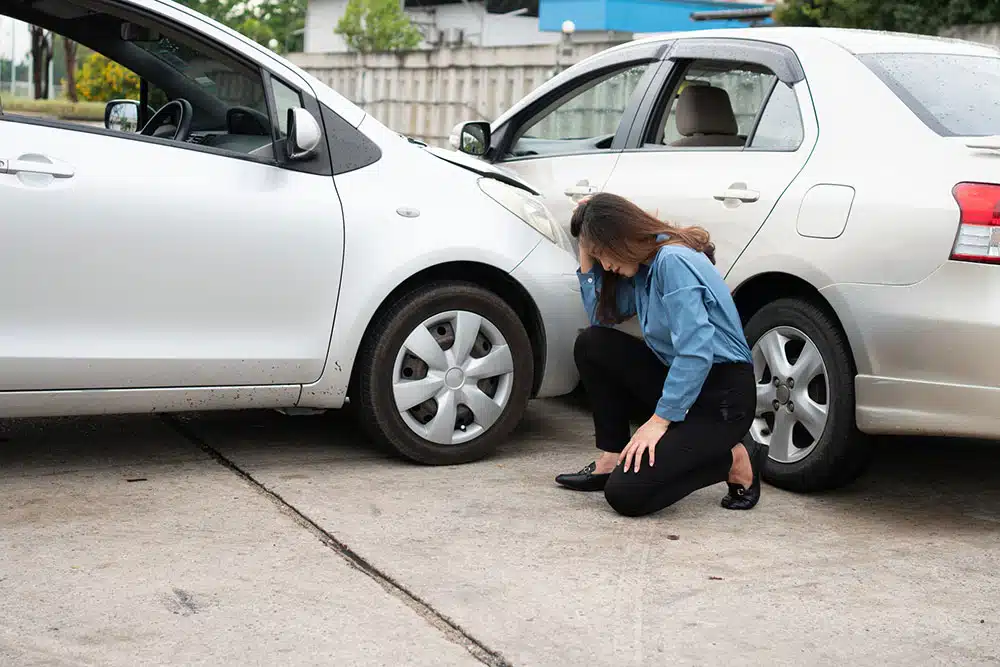 Woman looking upset beside a damaged car after a crash, illustrating how fault and comparative negligence affect car accident compensation in NYC.