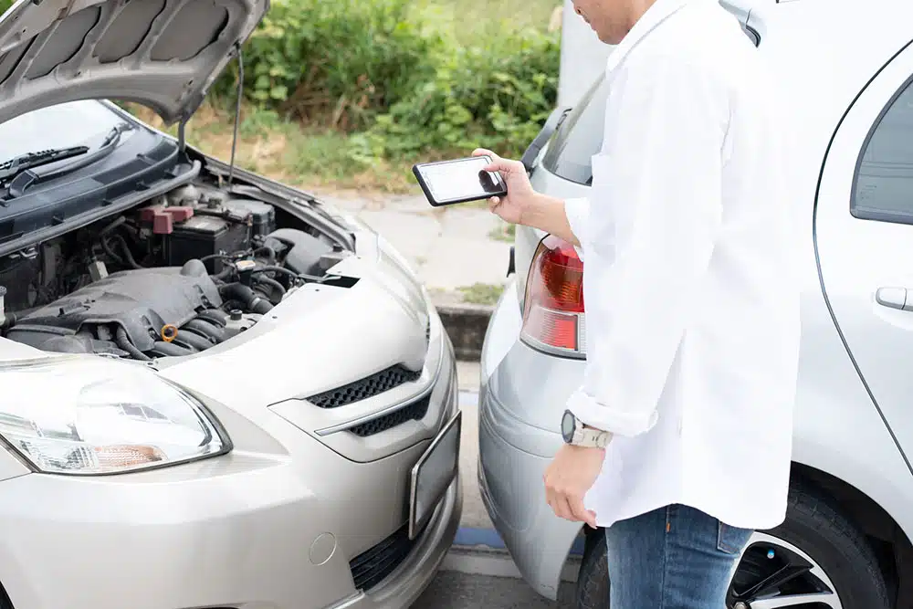 Driver inspecting car damage after a collision and preparing to send photos to the insurance company, representing how evidence impacts comparative negligence in NYC.