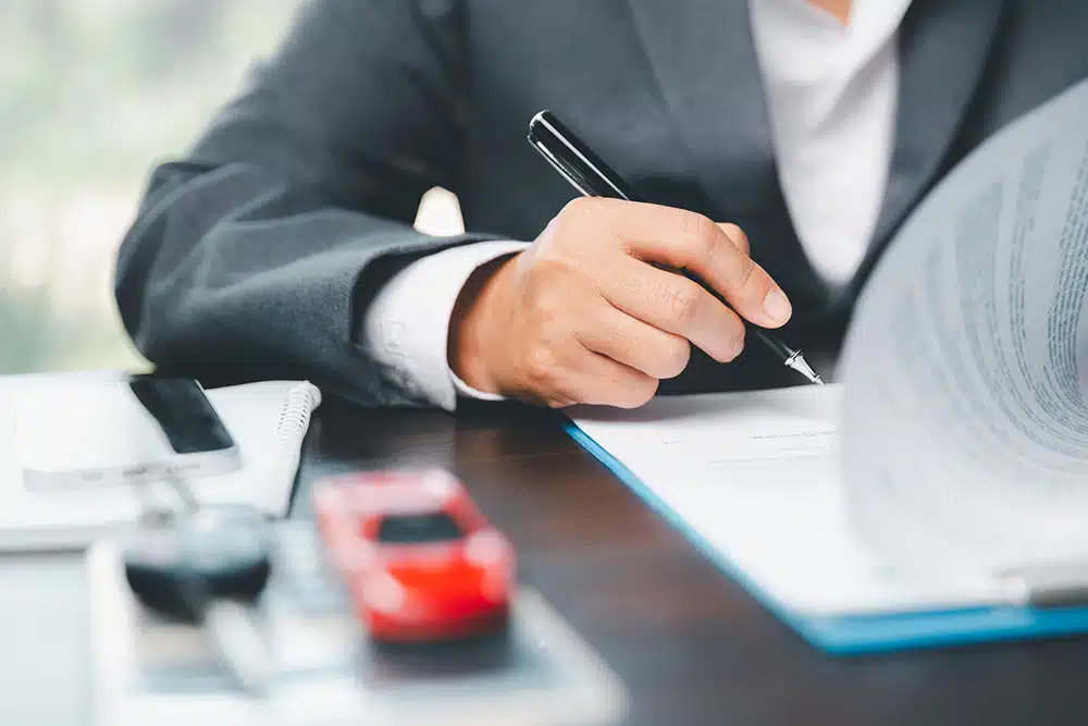 Person signing car insurance documents at a desk, symbolizing how comparative negligence rules in New York City affect car accident claims and settlements.