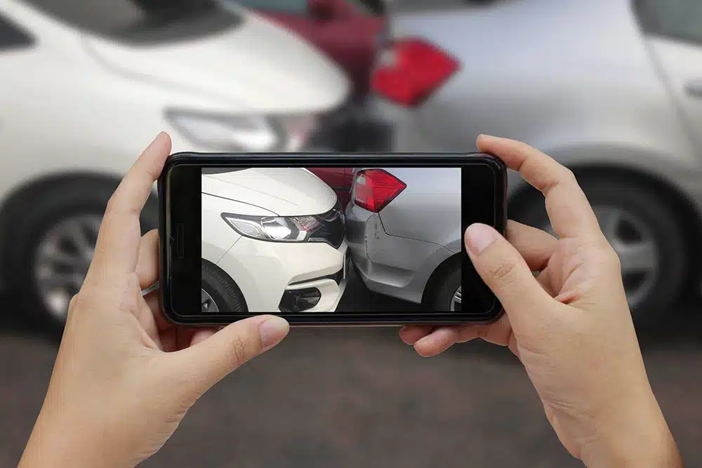 Hand holding a smartphone to photograph car crash damage, showing how evidence helps determine who is at fault in a rear-end accident.