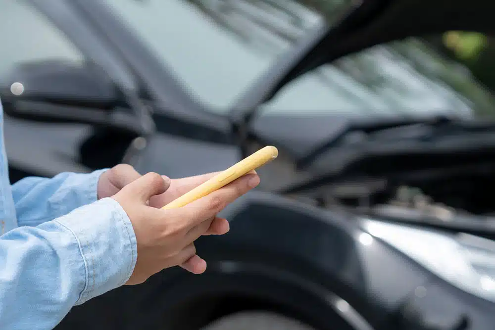 Woman using her phone beside a damaged car after a crash, illustrating how car accident lawyers handle insurance and claims while clients focus on recovery.